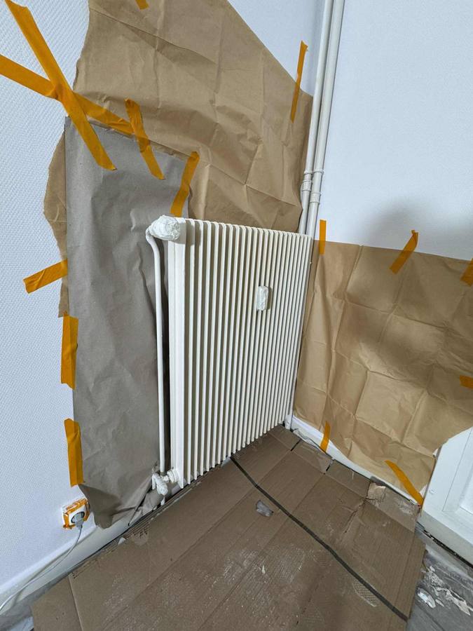 Radiateur protégé au papier et au ruban de masquage avant sa mise en peinture sur place à Besançon